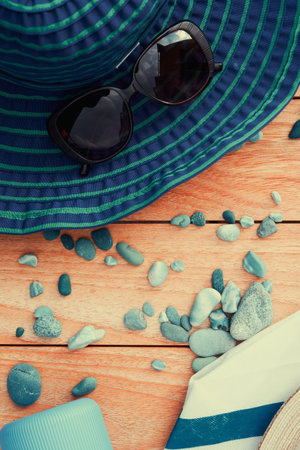 Big blue sun hat, bottle with cream, beach bag and pebbles on the wooden table. Sea holidays and vacation backgrounds. Vertical templateの写真素材