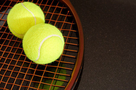Yellow tennis balls on brown racquet with new brown strings. Isolated on reflective black. Close up view. Recreational sports backgroundsの写真素材
