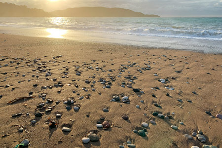 Sand beach with pebbles and tranquil sea water and bright sunset over mountains. Beautiful European...
