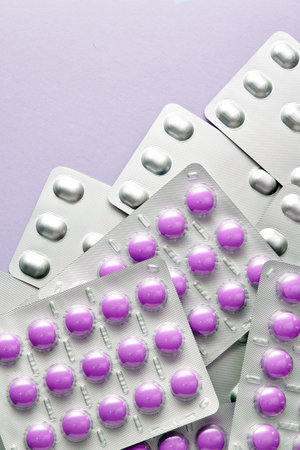 Close-up shot of purple pills in blister packs. The pills are arranged in a grid pattern and the...