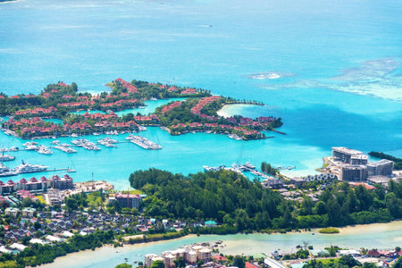 Aerial view of a tropical island with a marina full of boats, surrounded by lush greenery and beautiful blue water. Seychelles travel destinationsの写真素材