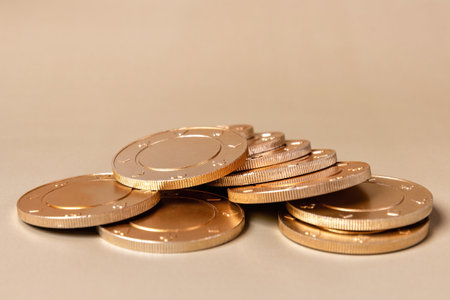 A close up of a heap of golden casino coins on a beige background. The chips are shiny and reflect light.の写真素材