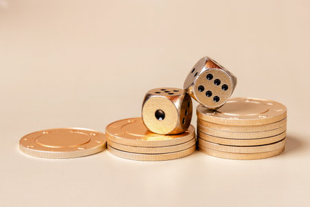 Two golden dice and stacks of gold casino coins on a light beige background. This image symbolizes luck, fortune, and wealth.の写真素材