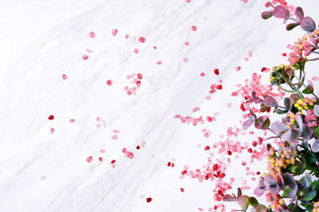 White marble surface is scattered with pink Himalayan salt crystals and adorned with a sprig of delicate flowers. Copy space for marketingの写真素材