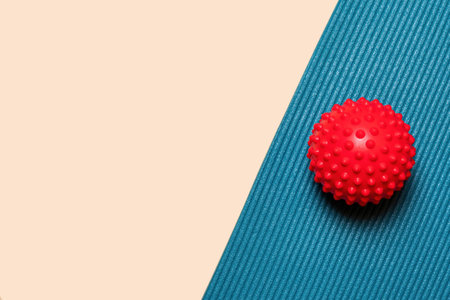 A red spiky massage ball sits on a blue yoga mat. The background is a light peach color. Copy space for marketing textの写真素材