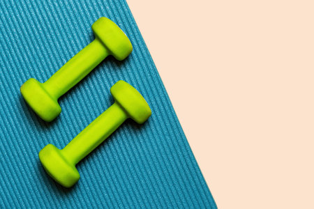 Two green dumbbells lay on a blue yoga mat. The dumbbells are perfect for home workouts. Copy space for marketing textの写真素材
