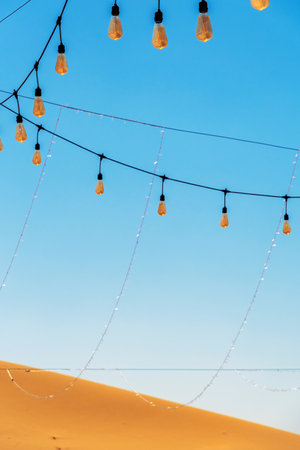 String lights hang against a clear blue sky, with a sandy desert dune in the foreground. Used natural elements to create a sense of calm and serenityの写真素材