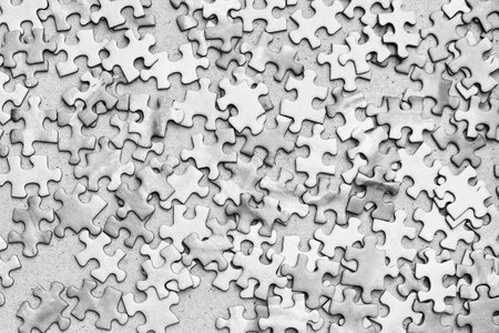 A close-up shot of scattered puzzle pieces in black and white. The pieces are arranged randomly, creating a sense of chaos and incompletenessの写真素材
