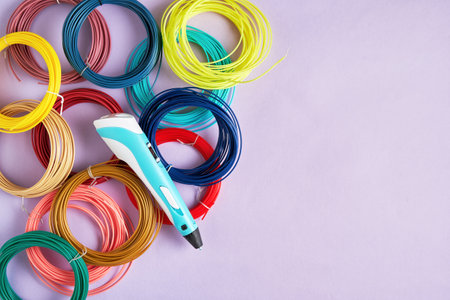 3D printing pen lies on a purple surface surrounded by colorful filament spools. Perfect for...
