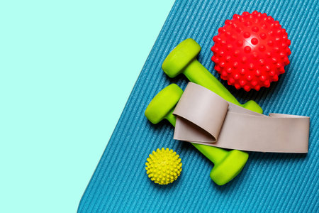 Vibrant flat lay showcasing a pair of lime green dumbbells, resistance band, and two massage balls arranged on a teal yoga matの写真素材