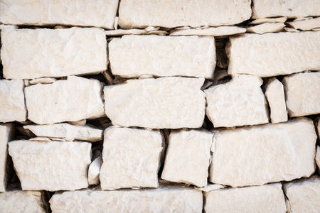 An image of a textured white stone wall showcases a pattern of rough-cut stones. Abstract natural backgroundsの写真素材