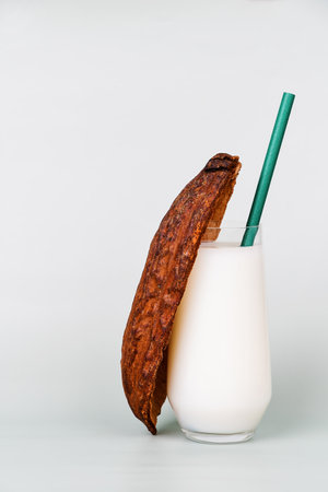 Glass of fresh milk is staged with a ripe cocoa pod and an eco-friendly straw. Connection between...