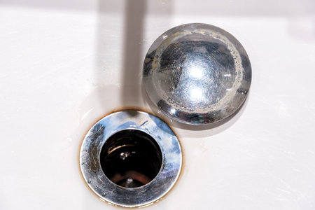 Top-down view of a worn and dirty bathroom sink with the broken stopper placed beside the drain