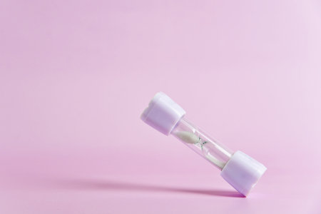Small white hourglass falling against a soft pink background, symbolizing time passing and the importance of deadlinesの写真素材