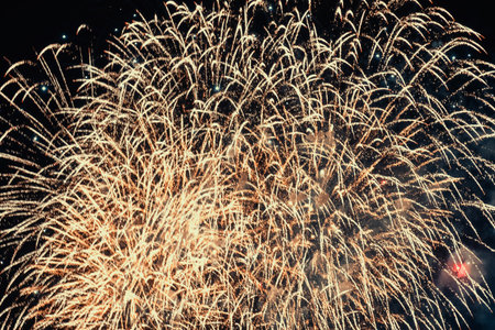 Large display of golden fireworks illuminates the night sky in a burst of celebration. Intricate...