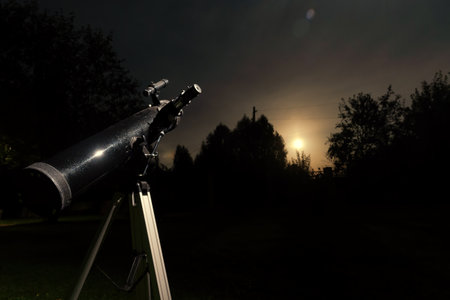Telescope in the darkness looking into luminous moon, inviting exploration of the night sky