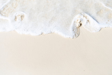 A close-up shot of a gentle wave washing over pristine white sand creates a serene and tranquil...