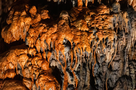 A close-up image shows orange-brown cave formations, highlighting the intricate details and textures created by water and minerals over timeの写真素材