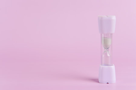 Minimalist hourglass on a light pink background. Concept of time running out and the urgency of...
