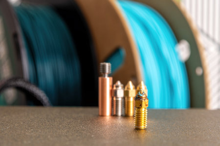 Set of new 3d printer nozzles and heat break and old nozzle on the table. Industrial equipment...