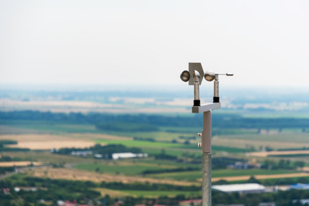 Close-up of an anemometer used for measuring wind speed, positioned on a hilltop with blurred fields and sky in the backgroundの写真素材