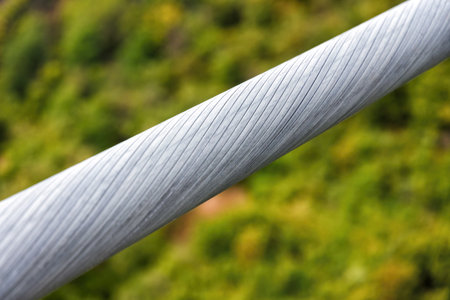 A close-up shot of a thick, metal cable with a blurred green background creates a sense of depth and...