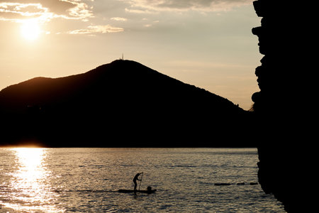 Silhouette of a person paddleboarding on the water at sunset, with a mountain in the background