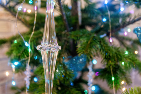 Elongated crystal ornament hangs on a decorated Christmas tree, bathed in the warm glow of colorful string lightsの写真素材