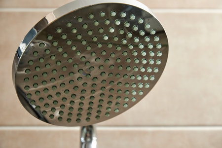 Detail of a modern, circular shower head with soft beige tiles in the background