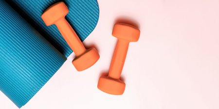 Vibrant orange dumbbells and blue yoga mat on pink, flat lay. Perfect for fitness, exercise, and wellness content. Ample copy spaceの写真素材
