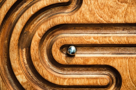 Top view of a wooden labyrinth puzzle with a silver ball in a track. Concept for strategy, navigating challenges, and business problem-solving