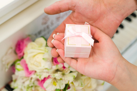 The bride and groom hold a closed, pink box with rings and a bouquet on the piano backgroundの写真素材