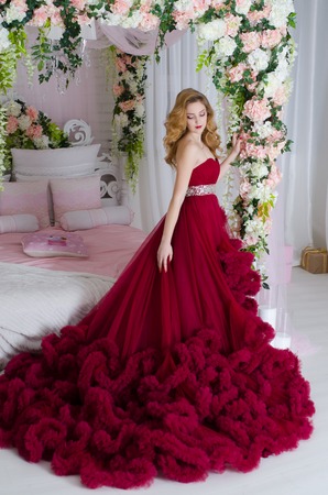 Charming woman in a beautiful lush dress cloud royal burgundy. It should be near the bed decorated with flowersの写真素材