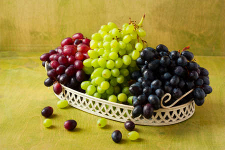 clusters of dark, red and green grapes on a white tray on a green wooden background horizontalの写真素材