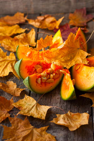 pumpkin cut into pieces on a wooden background strewn with autumn leavesの写真素材
