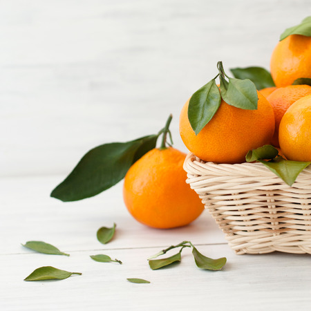 Fresh tangerines with green leaves in a wicker basket on a light wooden background. Natural style.の写真素材