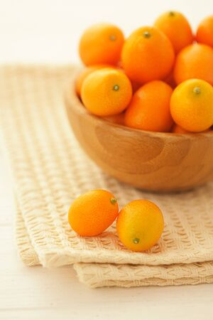Fresh kumquats in a wooden bowl on a table covered with a light cotton napkin. Vertical formatの写真素材