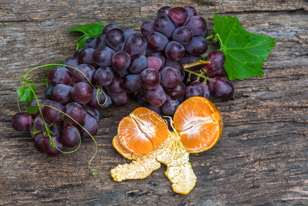 Bunches of fresh ripe red grapes and oranges on a wooden textural surface.の写真素材