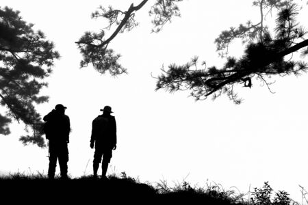 Silhouettes of two  travelers standing on Nok aen cliff on a white background at Phu Kradueng National park, a famous tourist destination in Thailand.の写真素材