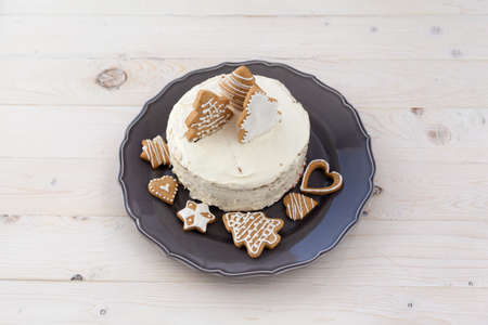 White cake with cookies in the shape of Christmas trees on a wooden white background