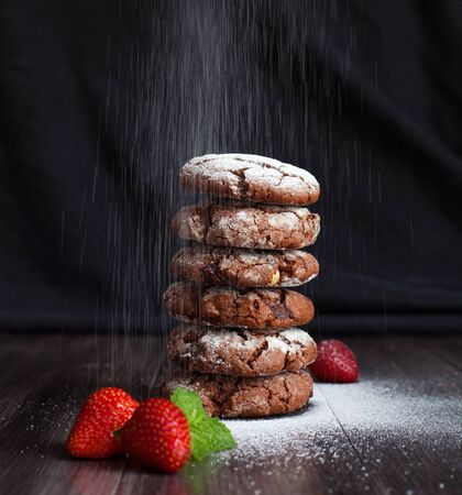 Delicious chocolate chip cookies, sprinkle with powdered sugar and a strawberry in the foreground. Cookies on a dark background.の写真素材