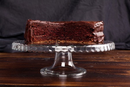 Sacher chocolate cake in a cut on a glass stand on a dark backgroundの写真素材