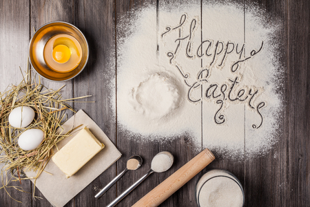 Ingredients for the dough for Easter. Eggs, flour, butter, sugar and kitchen tools on a dark wooden background. Rustic background with free text space. Flat lay. Top view.の写真素材