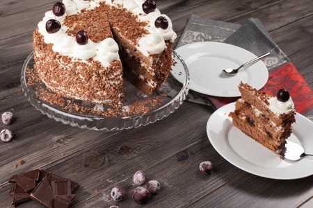 Black forest cake decorated with whipped cream, cherries and with chocolate chips on a dark wooden background.の写真素材