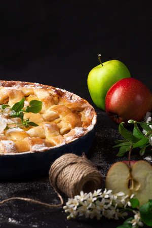 Delicious homemade rustic half-closed apple pie with fresh apples and apple-tree flowers on black background. Contrast vintage image.の写真素材