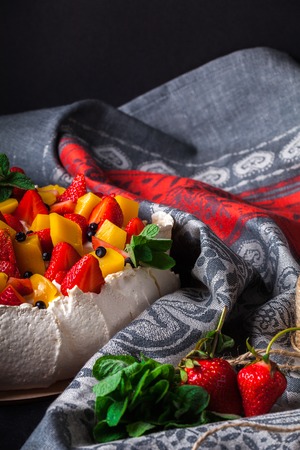 Snow-white meringue Pavlova Cake with fresh strawberries, slices of mango, blueberries and fresh mint on a dark background. Pavlova desert. Whipped cream cheese and mascarpone with berries and fruitsの写真素材