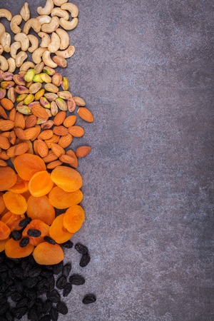 Dried fruit and nuts mixed and laid out on a dark background. Dried apricots, raisins, pistachios, almonds, cashew nuts on a dark background.の写真素材