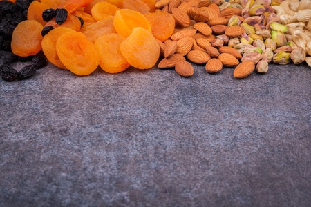 Dried fruit and nuts mixed and laid out on a dark background. Dried apricots, raisins, pistachios,...
