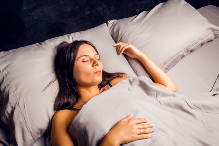 Woman sleeping in bed on a dark background. Beautiful young brunette sleeping sweetly in bed.