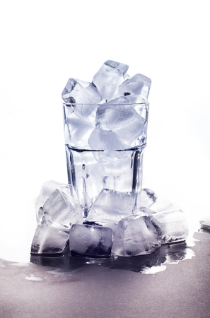 A glass with ice stands on a white background with a pile of ice cubes at the bottom. Chaotic scattered icicles . Winter background. New Year pattern.の写真素材